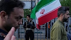 يقف أحد أفراد الأمن حارسًا بينما يحمل رجل العلم الإيراني خلال مسيرة نظمتها الدولة للاحتفال بعيد ميلاد الإمام رضا، الإمام الثامن للمسلمين الشيعة