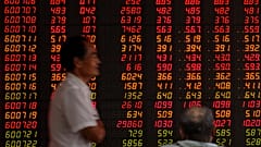 An investor walks by an electronic board displaying stock prices at a brokerage house in Beijing, October 2019.