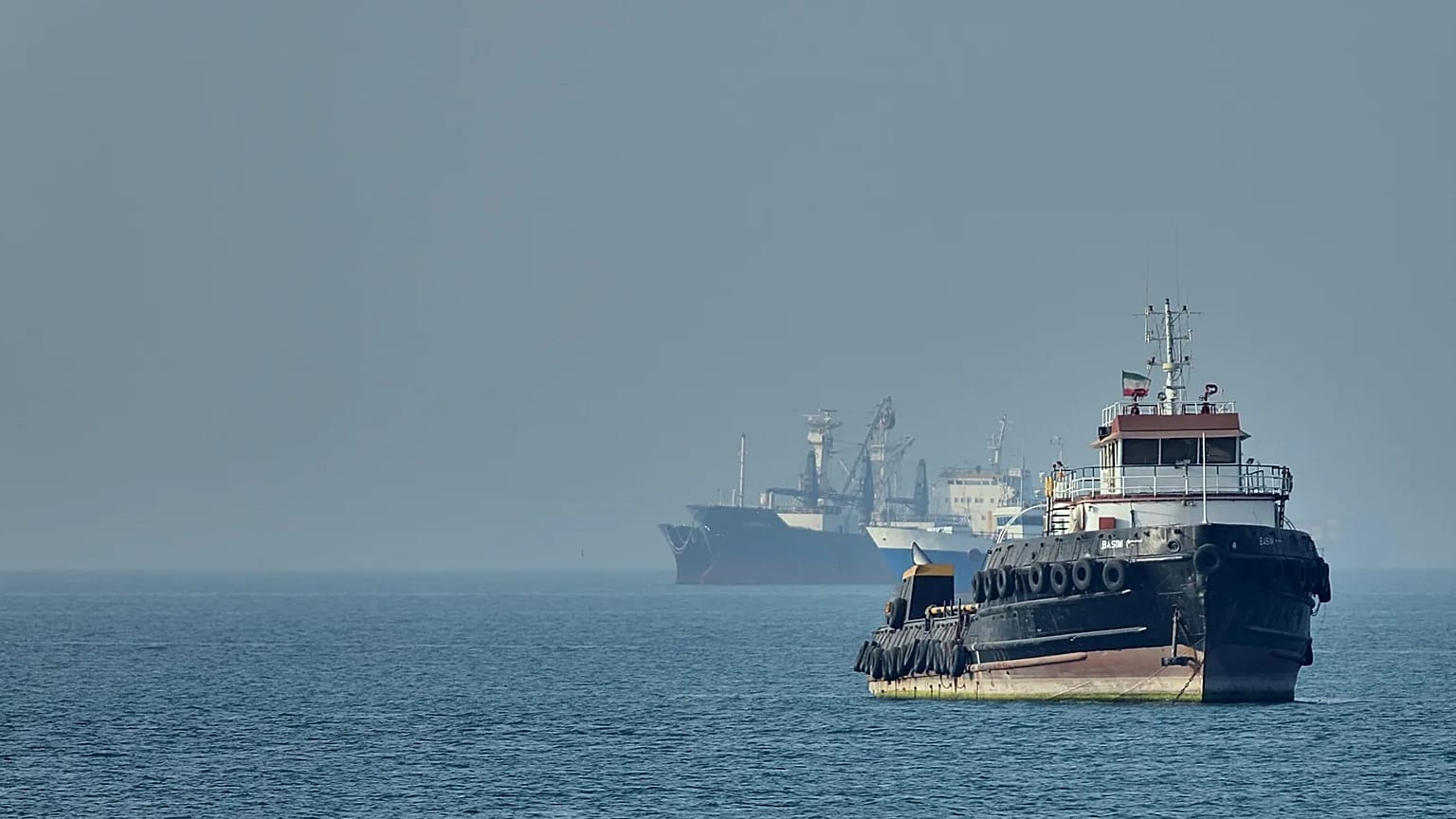 An Iranian tugboat floats in the foreground as cargo ships sit at anchor in the Strait of Hormuz off Bandar Abbas, 4 May, 2026