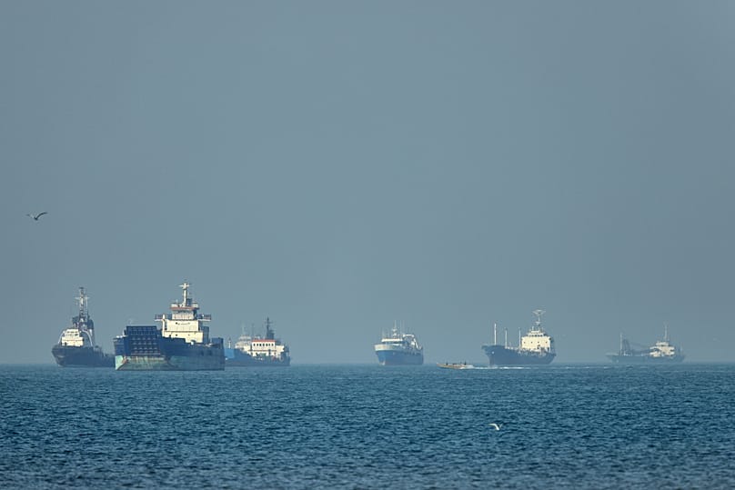 Cargo ships sit at anchor offshore as a small motorboat passes in the foreground, in the Strait of Hormuz off Bandar Abbas, Iran, Monday, May 4 , 2026.