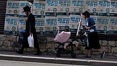 زوجان يهوديان متشددان يحملان مشترياتهما أثناء مرورهما أمام ملصقات الحملة الانتخابية للنائب الإسرائيلي اليميني المتطرف إيتامار بن غفير في بيت شيمش، إسرائيل، يوم الاثنين 24 أكتو