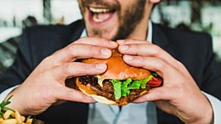 A man in a suit eating a burger. 