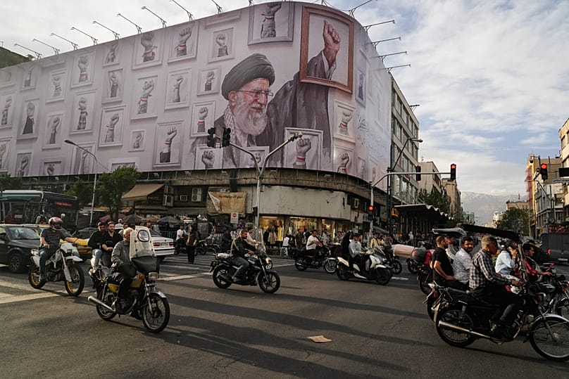 FILE: Motorbikes drive past a billboard with a graphic of the late Iranian Ayatollah Ali Khamenei, with his raised fist among his supporters, in downtown Tehran, 6 May 2026
