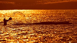 Eine Person spritzt am Freitag, dem 24. April 2026, bei Sonnenuntergang vor der Insel Poel in Deutschland Wasser auf einen gestrandeten Buckelwal.