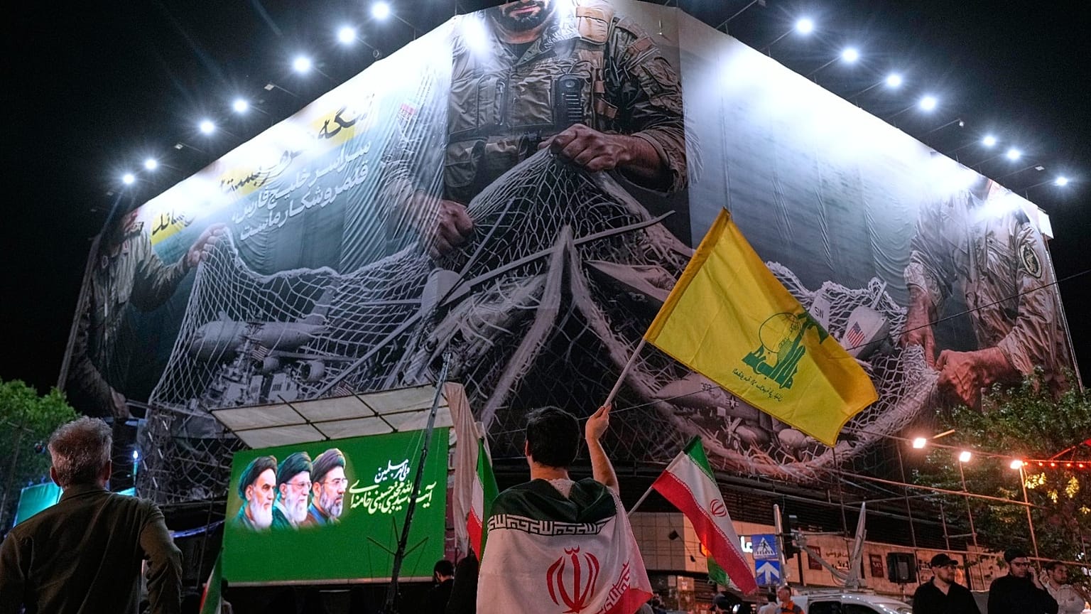 شخص يحمل أعلام حزب الله وإيران أمام لوحة إعلانية مناهضة للولايات المتحدة في ساحة انقلاب الإسلامي 4 مايو 2026