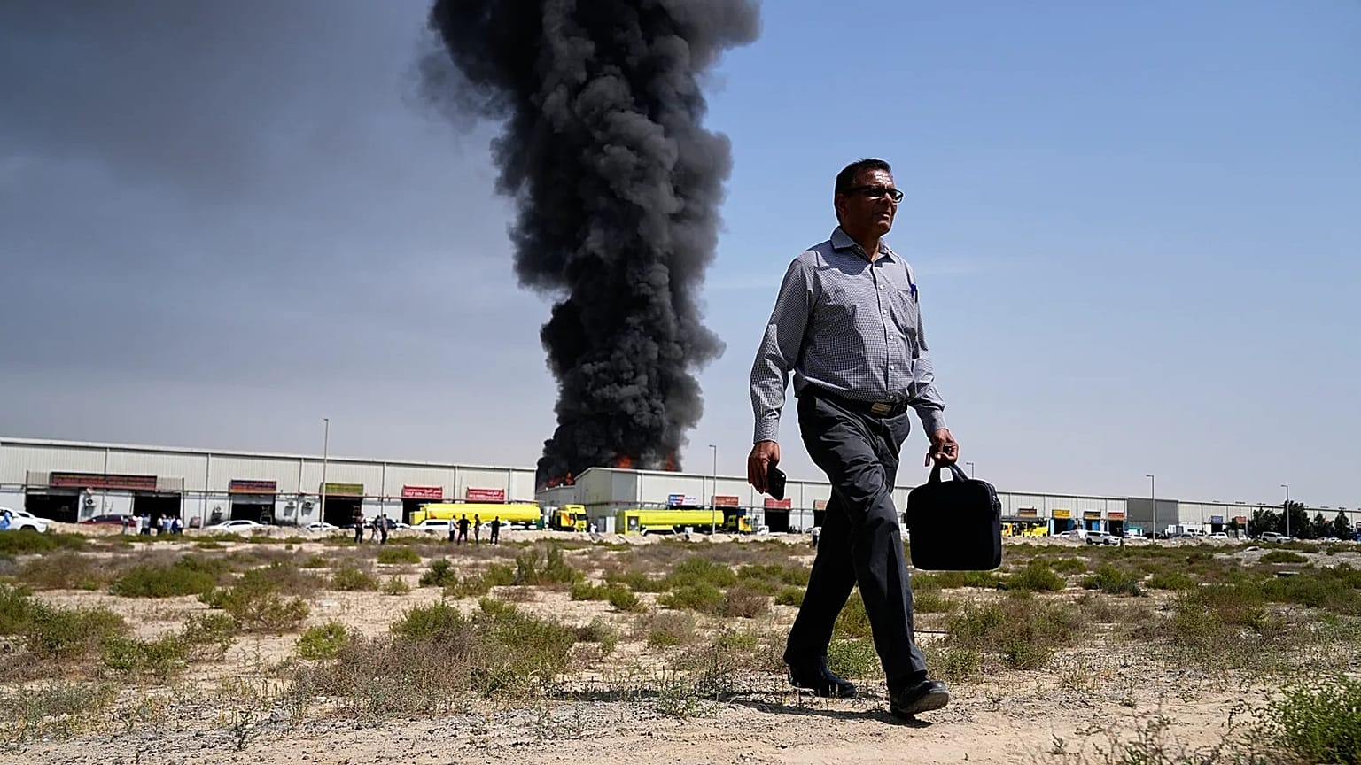 A man walks away after watching as a black plume of smoke rises from a warehouse in the industrial area of Sharjah City, 1 March, 2026