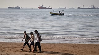 Children walk along the shore with bulk carriers and cargo ships in the Strait of Hormuz off Bandar Abbas, 27 April, 2026