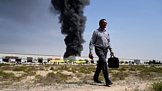 A man walks away after watching as a black plume of smoke rises from a warehouse in the industrial area of Sharjah City, 1 March, 2026