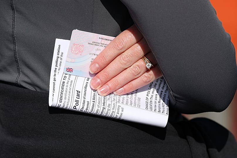 A voter holds a polling card as she queues at a polling station in Walton on the Naze, 7 May, 2026 