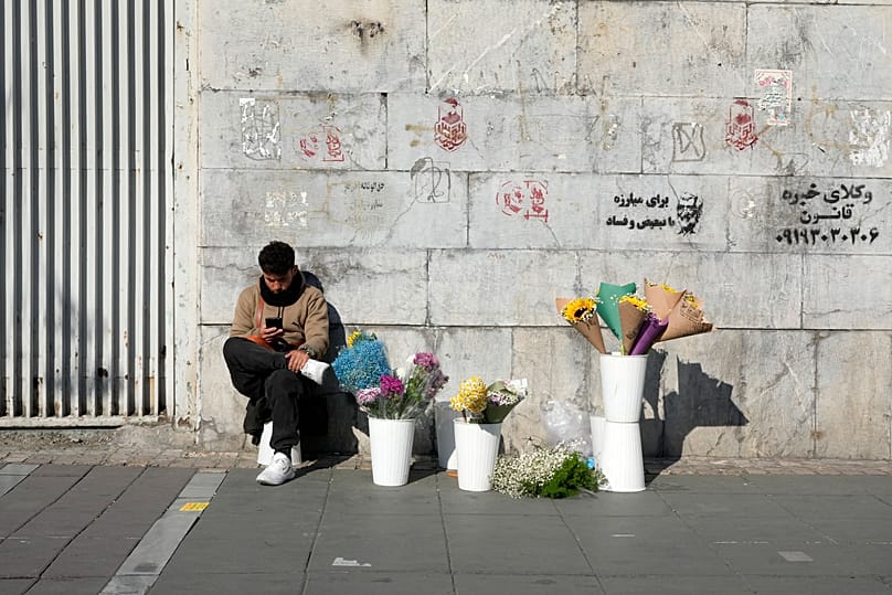 FILE: A street flower vendor looks at his phone at Enqelab-e-Eslami (Islamic Revolution) St. in downtown Tehran, 15 December 2024