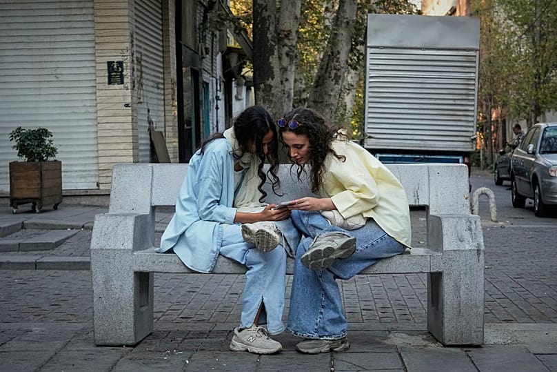 FILE: Two women chat while checking a smartphone in Tehran, 28 September 2025