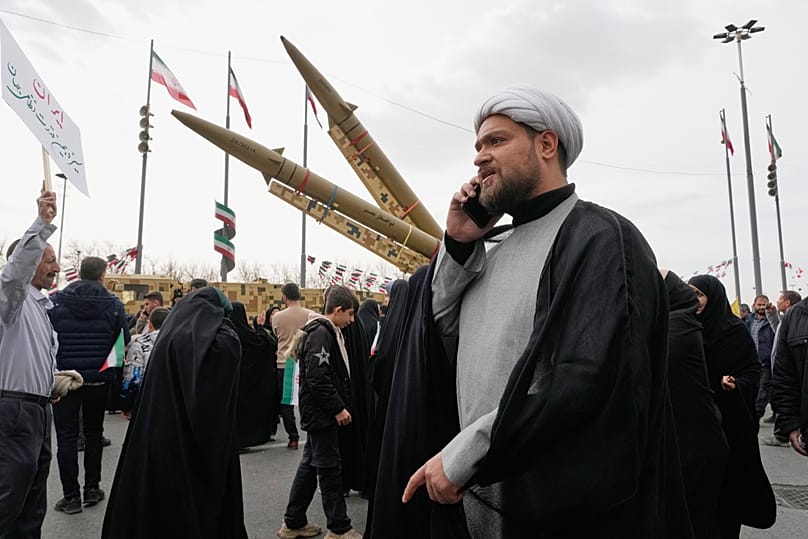 FILE: A cleric talks on his phone as he walks in front of missiles during an annual rally marking the Islamic Revolution at the Azadi square in Tehran, 11 February 2026