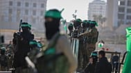 مقاتلو حماس يقفون على المسرح الذي سيتم فيه تسليم الرهينة الأمريكي الإسرائيلي كيث سيجل، 65 عامًا، إلى الصليب الأحمر في مدينة غزة