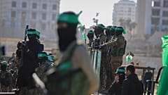 مقاتلو حماس يقفون على المسرح الذي سيتم فيه تسليم الرهينة الأمريكي الإسرائيلي كيث سيجل، 65 عامًا، إلى الصليب الأحمر في مدينة غزة