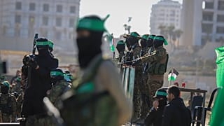 مقاتلو حماس يقفون على المسرح الذي سيتم فيه تسليم الرهينة الأمريكي الإسرائيلي كيث سيجل، 65 عامًا، إلى الصليب الأحمر في مدينة غزة
