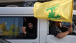 يحمل السكان النازحون علم حزب الله أثناء احتفالهم أثناء عودتهم إلى قراهم بعد وقف إطلاق النار بين إسرائيل وحزب الله