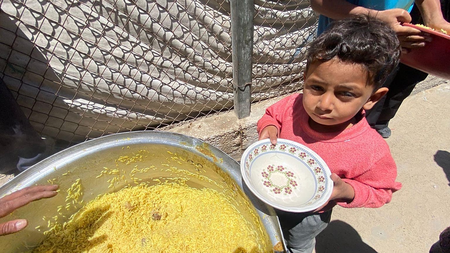 طفل من دير البلح ينتظر الحصول على بعض من الأرز الذي أعدته إحدى التكايا (المطابخ الخيرية) 