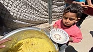 طفل من دير البلح ينتظر الحصول على بعض من الأرز الذي أعدته إحدى التكايا (المطابخ الخيرية) 