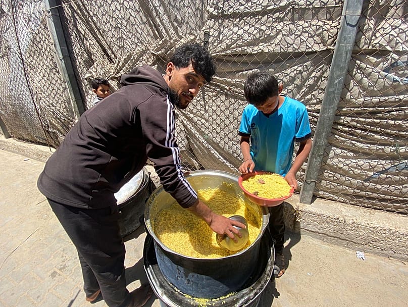 عامل في إحدى التكايا يوزع وجبة من الأرز على أطفال نازحين وسط قطاع غزة