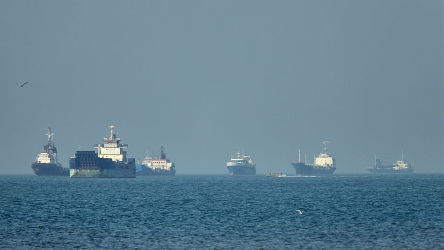Navi cargo alla fonda al largo nello stretto di Hormuz, di fronte a Bandar Abbas in Iran, mentre una piccola barca a motore passa in primo piano, lunedì 4 maggio 2026.