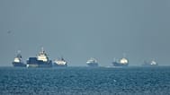 Cargo ships sit at anchor offshore as a small motorboat passes in the foreground, in the Strait of Hormuz off Bandar Abbas, Iran, Monday, May 4, 2026