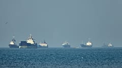 Cargo ships sit at anchor offshore as a small motorboat passes in the foreground, in the Strait of Hormuz off Bandar Abbas, Iran, Monday, May 4, 2026