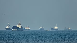 Cargo ships sit at anchor offshore as a small motorboat passes in the foreground, in the Strait of Hormuz off Bandar Abbas, Iran, Monday, May 4, 2026