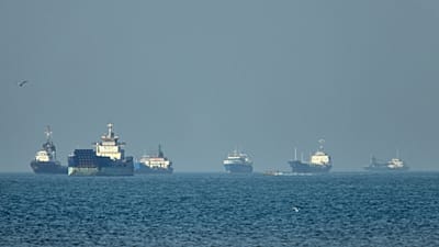 Cargo ships sit at anchor offshore as a small motorboat passes in the foreground, in the Strait of Hormuz off Bandar Abbas, Iran, Monday, May 4, 2026