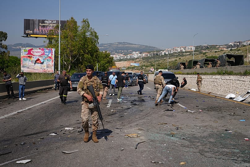 Security forces and residents inspect and clear debris scattered across a road at the scene of an Israeli airstrike that hit a car in the coastal town of Saadiyat.