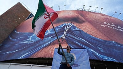 A man waves an Iranian flag under a billboard with graphic showing Strait of Hormuz and sewn lips of US President Donald Trump in downtown Tehran, Wednesday, May 6, 2026.