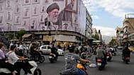 تمر الدراجات النارية أمام لوحة إعلانية عليها رسم يظهر المرشد الأعلى الإيراني الراحل آية الله علي خامنئي