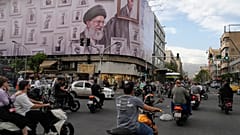تمر الدراجات النارية أمام لوحة إعلانية عليها رسم يظهر المرشد الأعلى الإيراني الراحل آية الله علي خامنئي
