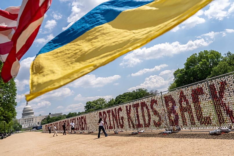 Demonstrators wave American and Ukrainian flags as thousands of teddy bears representing children deported from Ukraine by Russia are displayed in Washington, 23 April, 2026