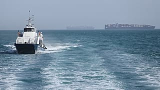 FILE: A patrol boat moves through the water as cargo ships sit at anchor in the Strait of Hormuz off Bandar Abbas, 2 May 2026