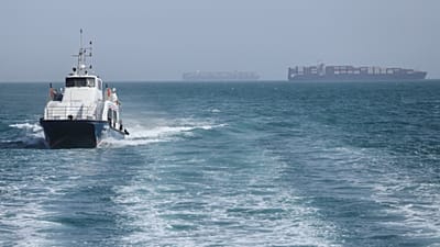 FILE: A patrol boat moves through the water as cargo ships sit at anchor in the Strait of Hormuz off Bandar Abbas, 2 May 2026