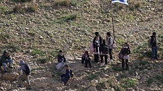 Palestinian students walk to school along a fence separating their village from a nearby Israeli settlement of Carmel, which forces them to take an alternative route nearly tw
