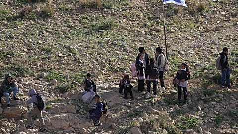 Palestinian students walk to school along a fence separating their village from a nearby Israeli settlement of Carmel, which forces them to take an alternative route nearly tw
