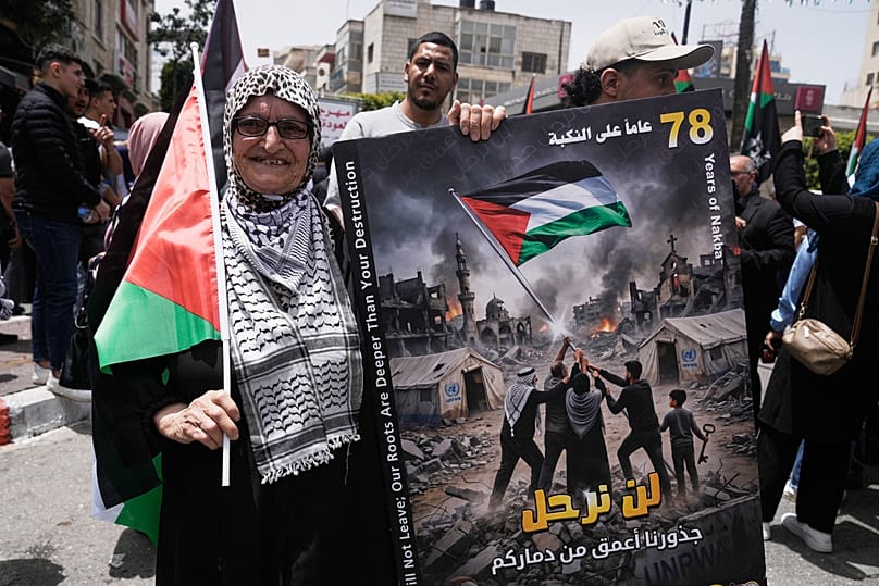امرأة فلسطينية مسنّة تحمل لافتة كُتب عليها "لن نرحل.. جذورنا أعمق من دماركم" خلال فعالية لإحياء الذكرى الـ78 للنكبة في رام الله، في 12 مايو 2026.