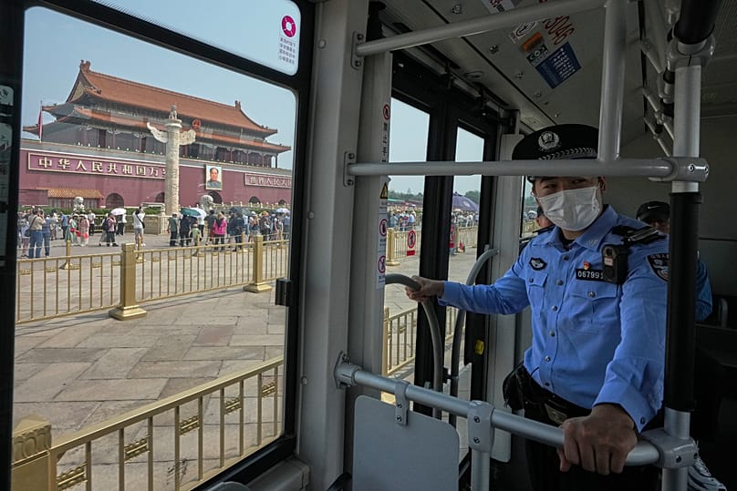 A policeman stands watch as commuters ride on a bus past Tiananmen Gate in Beijing, 13 May, 2026
