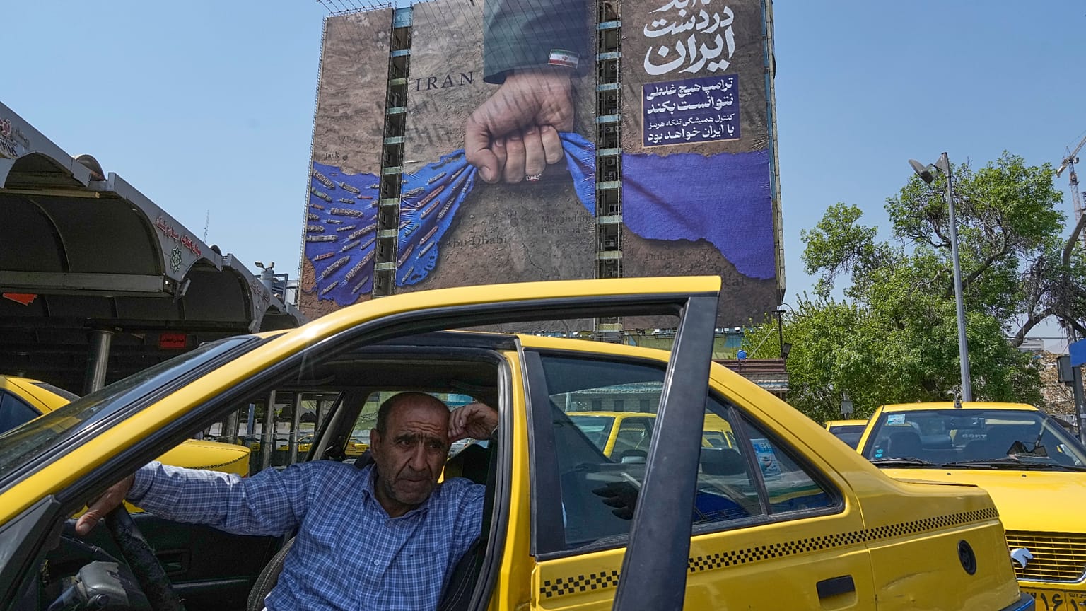 سائق سيارة أجرة ينتظر ركابًا أمام لوحة إعلانية شمال طهران، إيران، الخميس 16 نيسان/أبريل 2026. 