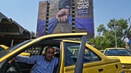 سائق سيارة أجرة ينتظر ركابًا أمام لوحة إعلانية شمال طهران، إيران، الخميس 16 نيسان/أبريل 2026. 