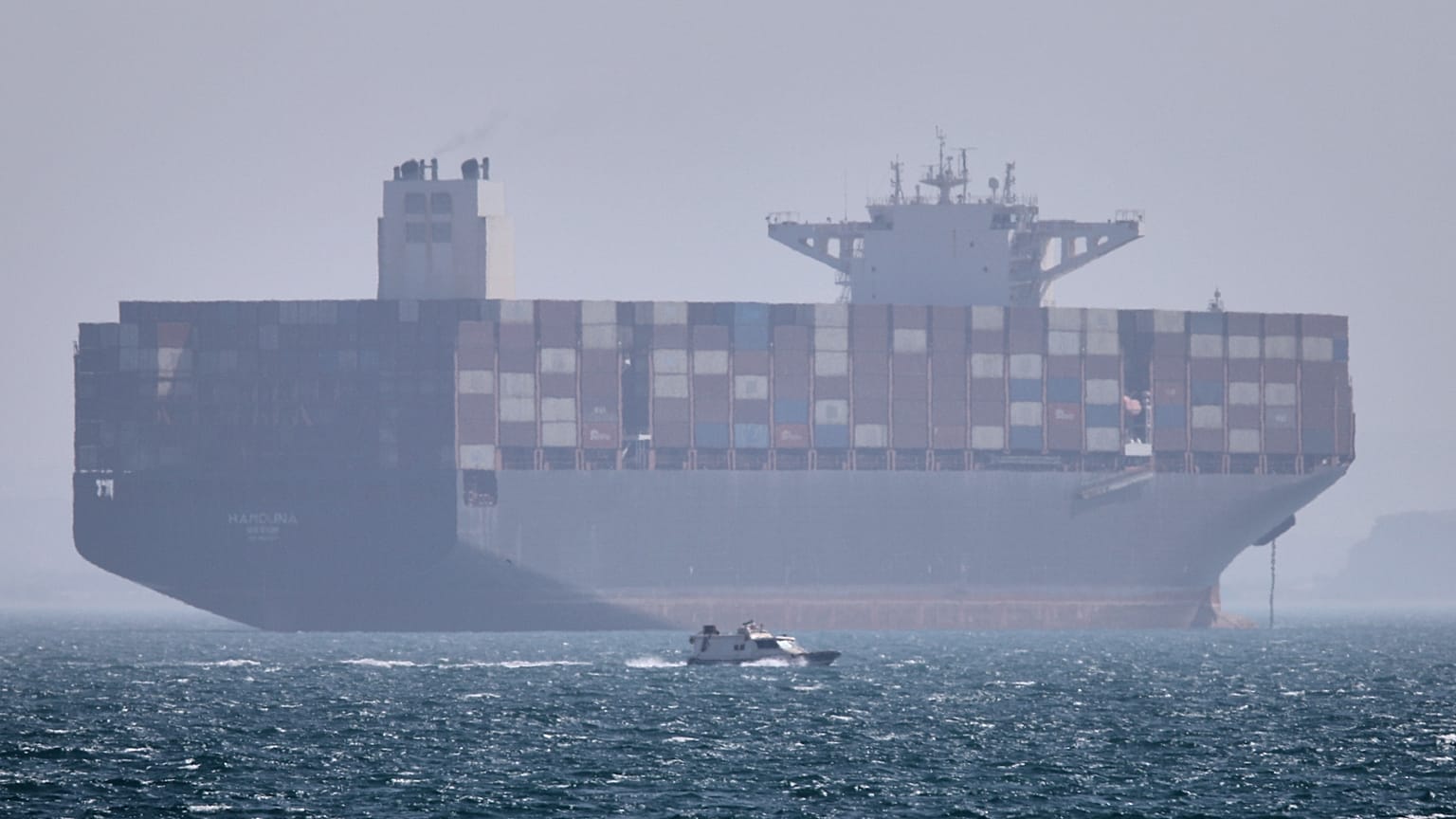 FILE: A container ship sits at anchor as a small motorboat passes in the foreground in the Strait of Hormuz off Bandar Abbas, 2 May 2026