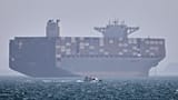 FILE: A container ship sits at anchor as a small motorboat passes in the foreground in the Strait of Hormuz off Bandar Abbas, 2 May 2026