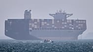FILE: A container ship sits at anchor as a small motorboat passes in the foreground in the Strait of Hormuz off Bandar Abbas, 2 May 2026