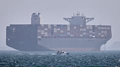 DATEI: Ein Containerschiff liegt vor Anker, während im Vordergrund ein kleines Motorboot in der Straße von Hormuz vor Bandar Abbas vorbeifährt, 2. Mai 2026