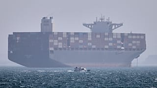 DATEI: Ein Containerschiff liegt vor Anker, während im Vordergrund ein kleines Motorboot in der Straße von Hormuz vor Bandar Abbas vorbeifährt, 2. Mai 2026