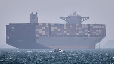 FILE: A container ship sits at anchor as a small motorboat passes in the foreground in the Strait of Hormuz off Bandar Abbas, 2 May 2026
