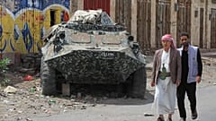 أشخاص يسيرون بجوار دبابة دمرتها غارات جوية للتحالف بقيادة السعودية في عام 2015، خلال حدث لإحياء الذكرى التاسعة للغارات الجوية، في صنعاء، اليمن، الخميس 26 مارس 2026