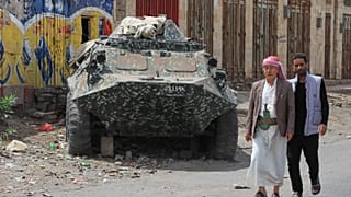 أشخاص يسيرون بجوار دبابة دمرتها غارات جوية للتحالف بقيادة السعودية في عام 2015، خلال حدث لإحياء الذكرى التاسعة للغارات الجوية، في صنعاء، اليمن، الخميس 26 مارس 2026
