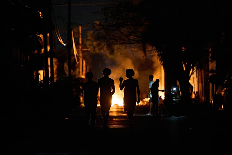 People walk down the street next to a fire set up by residents protesting against prolonged power outages on the street in Havana, 14 May, 2026